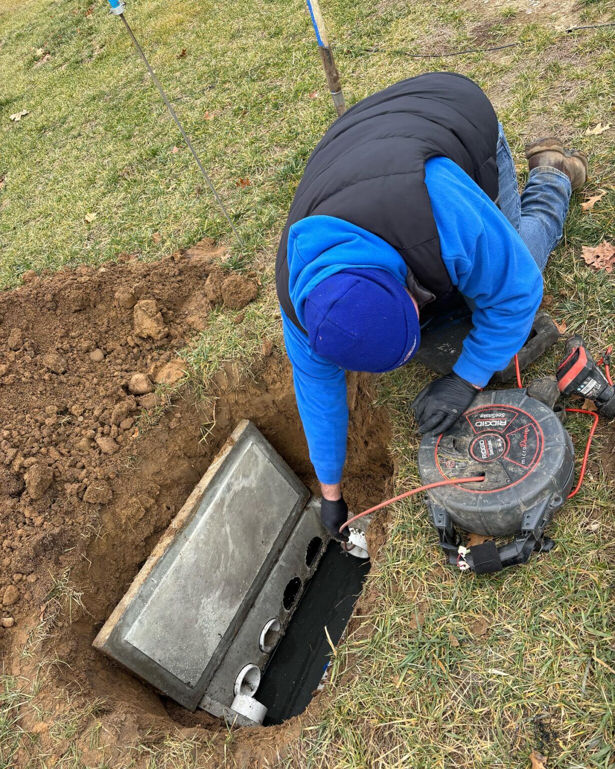468086931_18345583543122526_487978378969194033_n - ARWWM - ARWWM Worker kneeling beside a trench, measuring and placing concrete forms for a pipe installation with a drill nearby on grassed ground - arwwm - arwwm