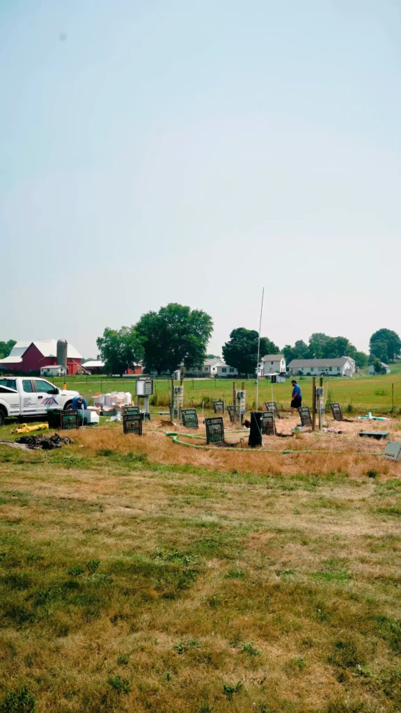 Commercial Wastewater Services - ARWWM - ARWWM Field with scattered chairs and equipment in the foreground, a person walking near utility posts, farm buildings in the background. - arwwm - arwwm