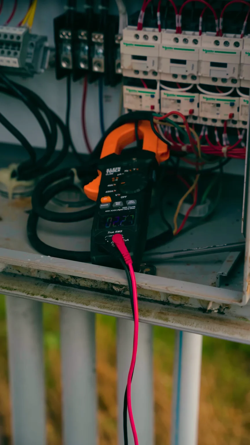 Digital multimeter connected to an electrical panel, measuring voltage across red and black probes amid fanned wiring and breakers. - arwwm - arwwm