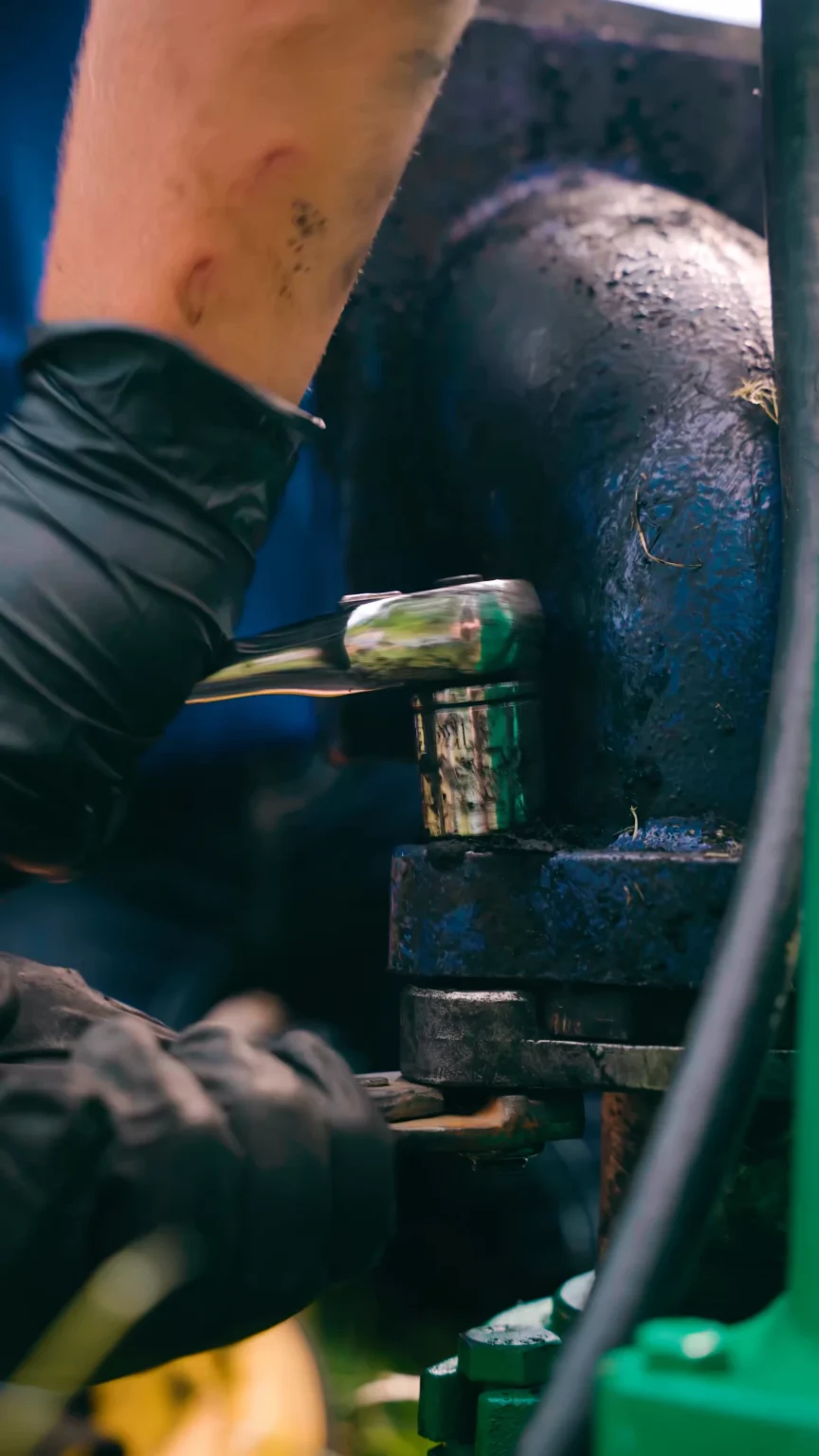 Pump Repair - ARWWM - ARWWM Close-up of a gloved hand tightening a bolt on blue-green industrial machinery - arwwm - arwwm
