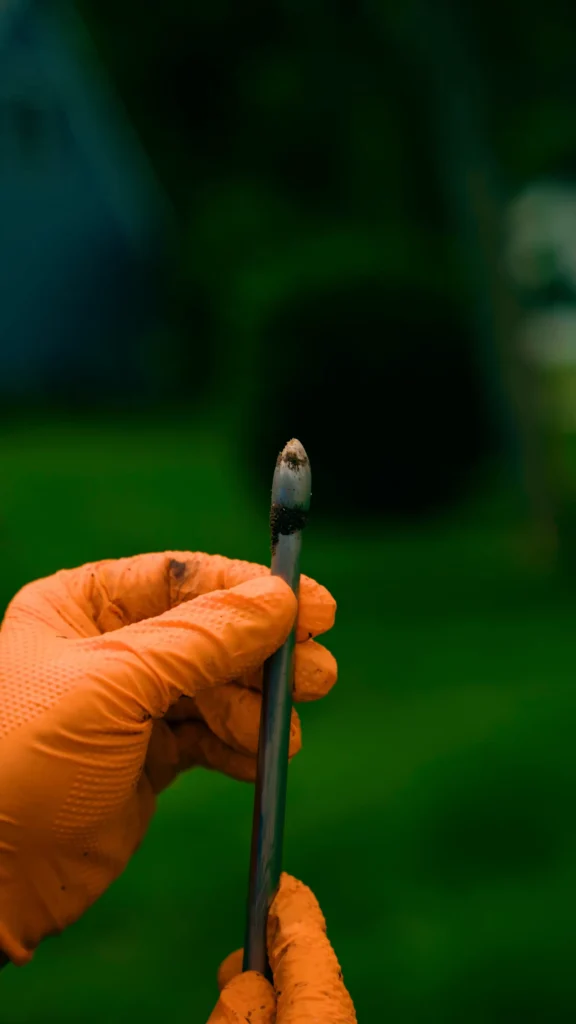 Gloved hand holding a small lab tool with soil on the tip, outdoors in a green background - arwwm - arwwm