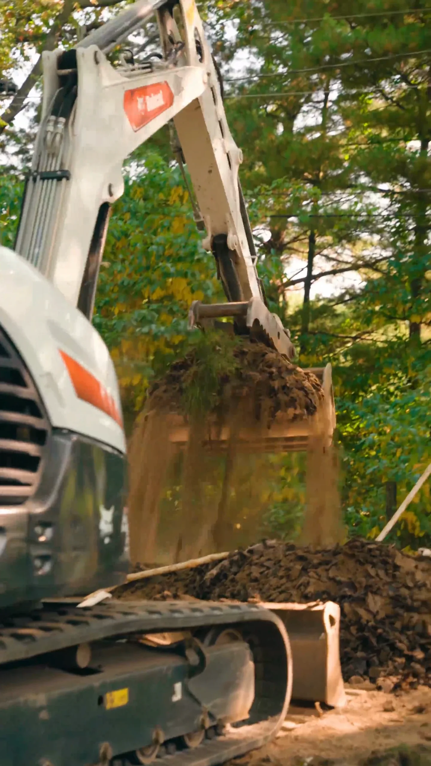Excavator bucket dumping soil into a dump truck at a construction site with trees in the background. - arwwm - arwwm