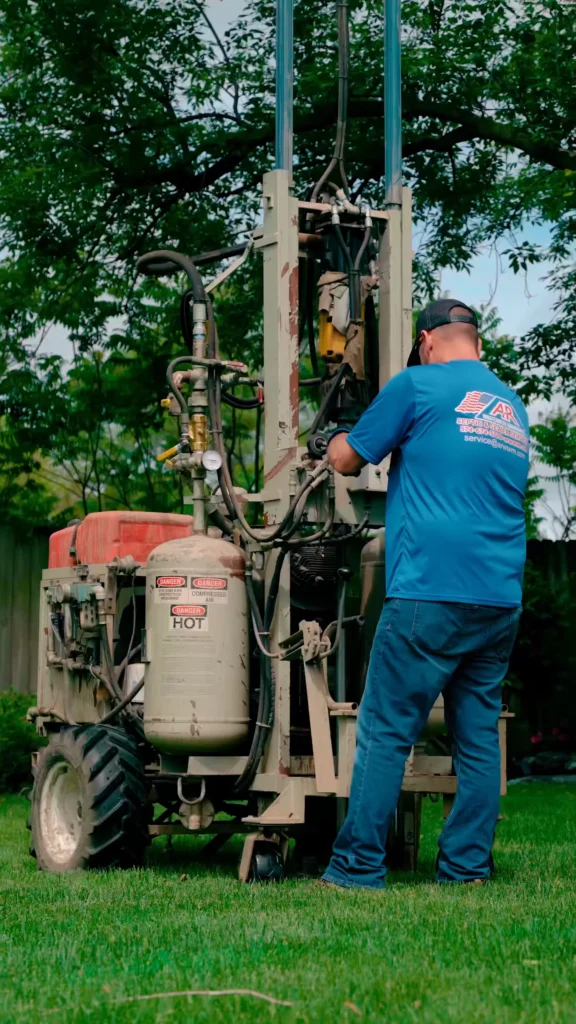 Terralifting - ARWWM - ARWWM Worker in blue shirt and cap operating a weathered drilling rig outdoors on a grassy lawn - arwwm - arwwm